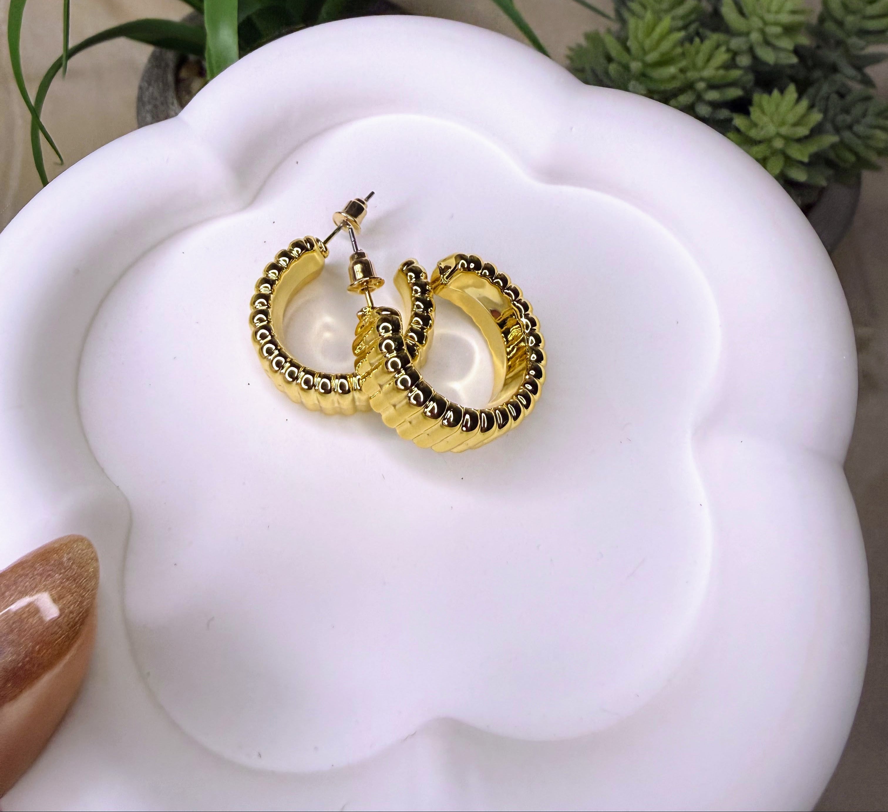 Gold hoop earrings on a white floral stand with plants in the background