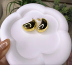 Gold earrings on a white surface with a plant in the background