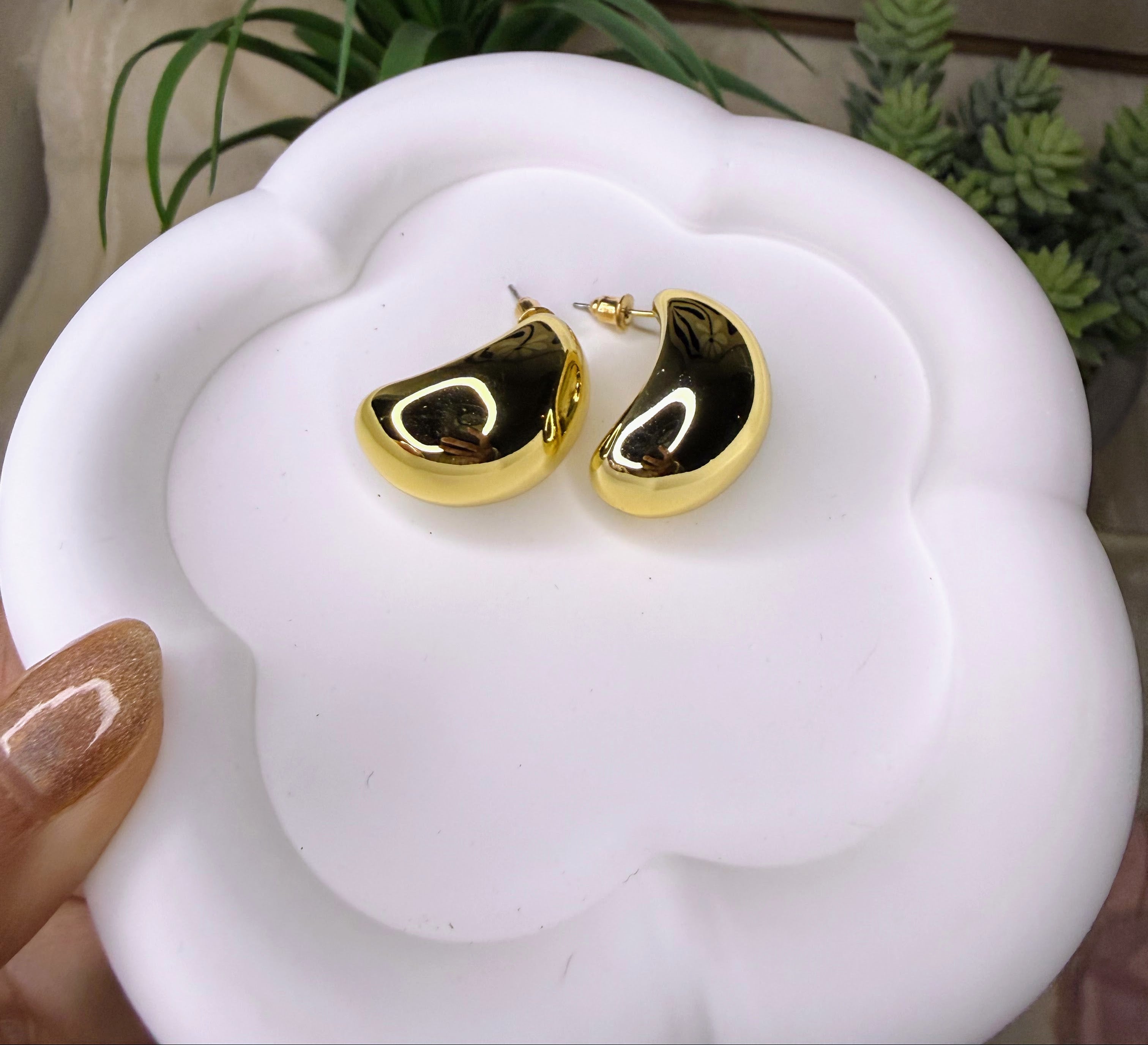 Gold earrings on a white surface with a plant in the background