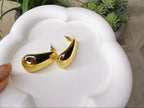 Gold hoop earrings on a white surface with plants in the background